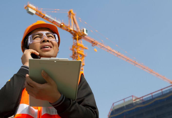 Construction site manager holding the ANSI/ASSP A10.28-2018 document and asking about work platforms suspended by cranes.