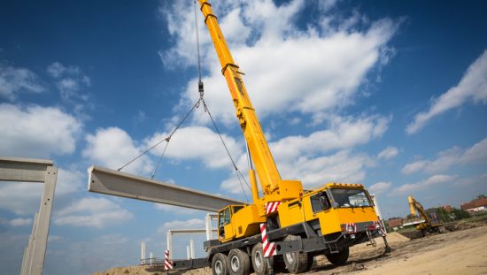 Bright yellow ASME B30.5-2018 mobile crane lifting in action
