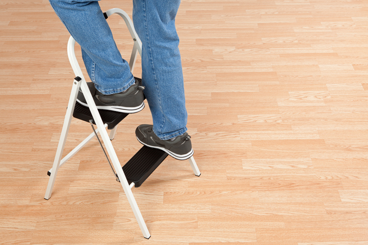 Two feet finding their way up a stepladder by safely following the ANSI ASC A14.11-2018 standard on a wooden floor