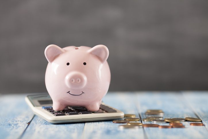 Piggy bank on a calculator next to loose change to symbolize ISO 55002