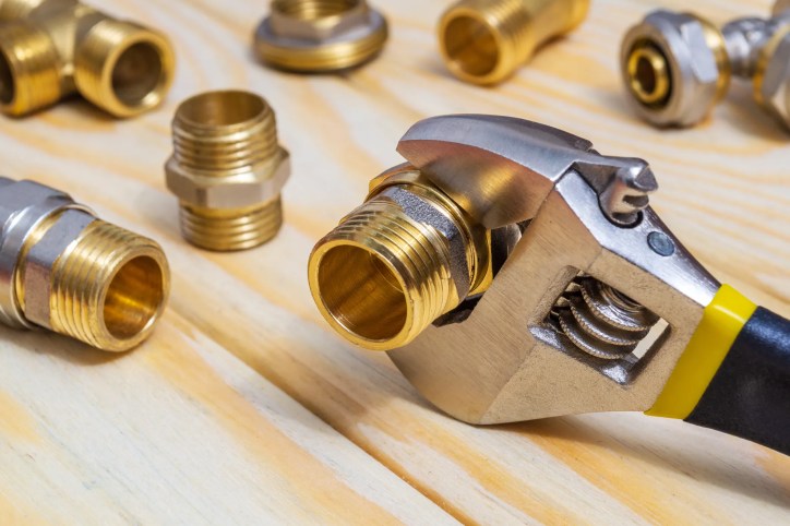 Wrench holding gold plumbing supply fillings on wood board through ASME A112.18.1-2018