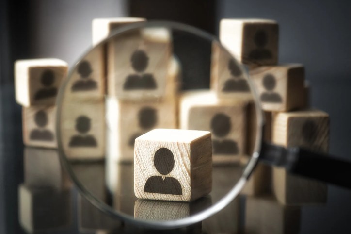 Stacked wooden blocks with an icon representing a person on them. One block is brought into view with a magnifying glass which represents protecting personally identifiable information as specified in ISO/IEC 27018.