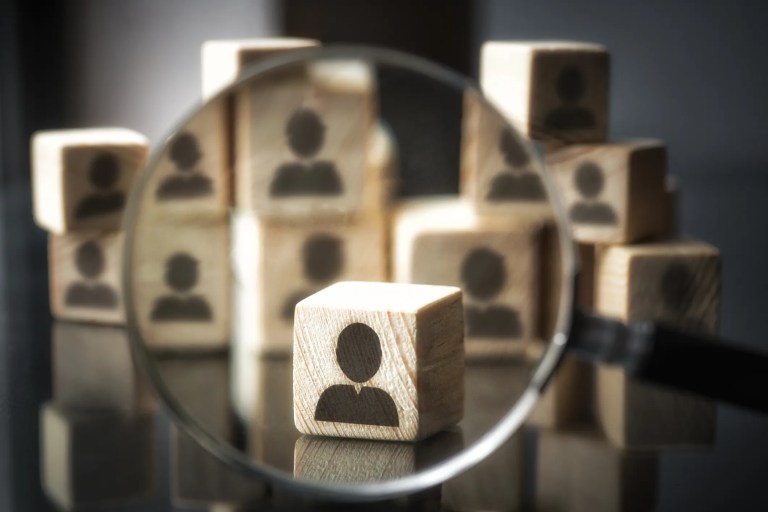 Stacked wooden blocks with an icon representing a person on them. One block is brought into view with a magnifying glass which represents protecting personally identifiable information as specified in ISO/IEC 27018.