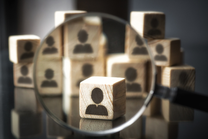 Stacked wooden blocks with an icon representing a person on them. One block is brought into view with a magnifying glass which represents protecting personally identifiable information as specified in ISO/IEC 27018.