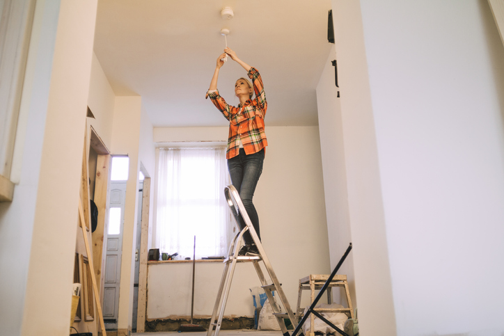 A woman safely operating a stepladder at home to change a lightbulb.