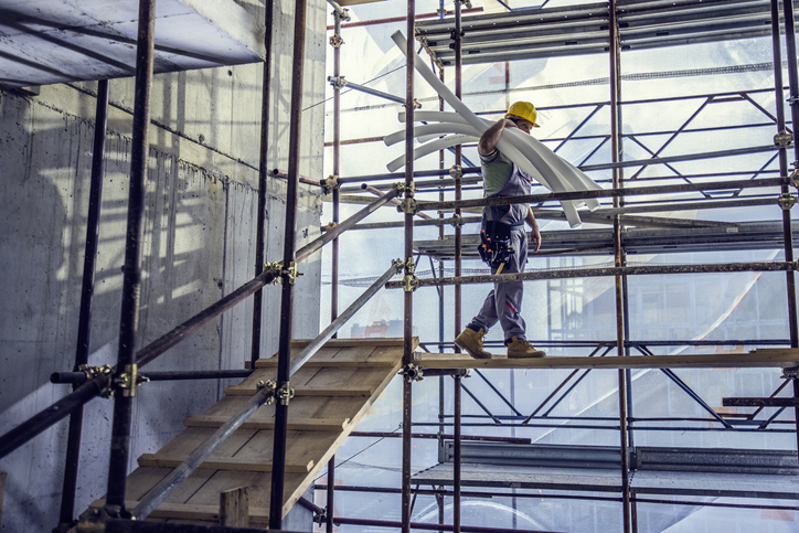 Construction worker safely slugging white piping on ANSI/ASSP A10.8-2019 scaffolding