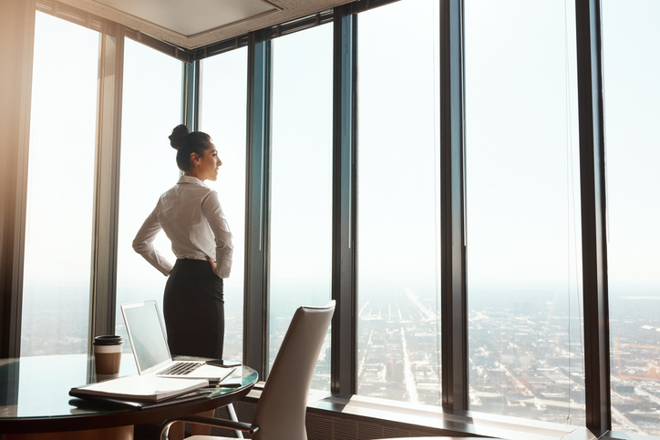 Businesswoman gazing out window, pleased to have completed an onsite visit and become ANSI/ISO/IEC 17024 accredited.