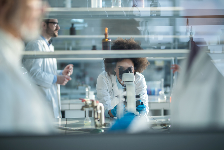 Scientist using root cause analysis via ISO/IEC 17025 to examine sample in microscope.