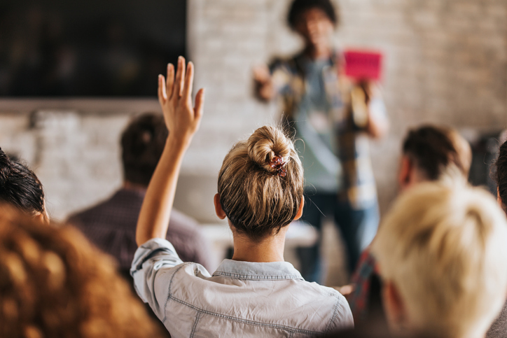 Woman raising her hand in class and gaining the benefits of training outlined in ISO standards.