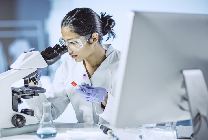 Woman examining microscopic sample and following updates to standards based on last ISO/IEC 17025 edition.
