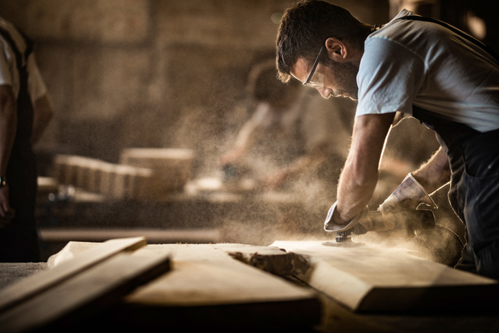 Man working hard sanding wood while preventing fire and dust explosions with NFPA 654-2020.