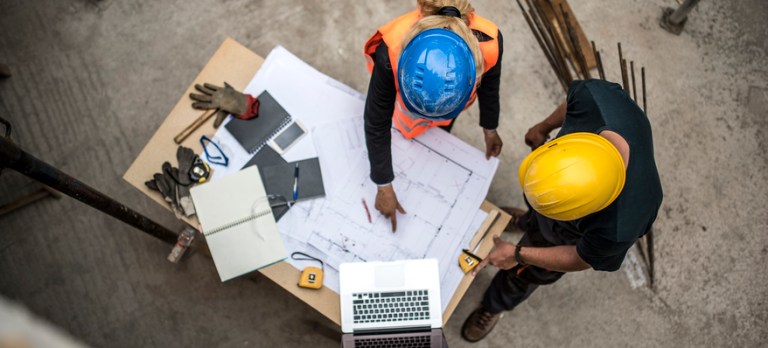 Overhead view of two construction workers discussing over a blueprint