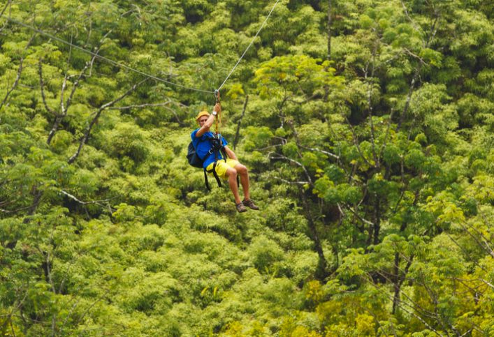Adventure seeker sliding across ASTM F2959-19 zip line in the trees.