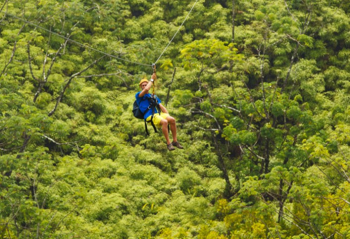 Adventure seeker sliding across ASTM F2959-21 zip line in the trees.