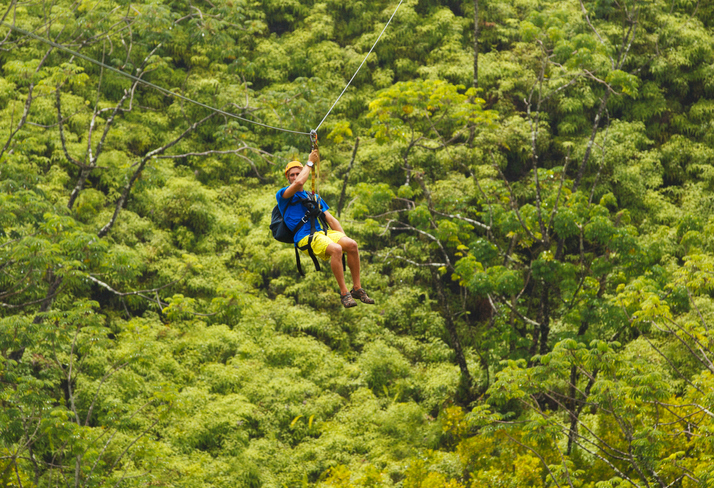 Adventure seeker sliding across ASTM F2959-21 zip line in the trees.