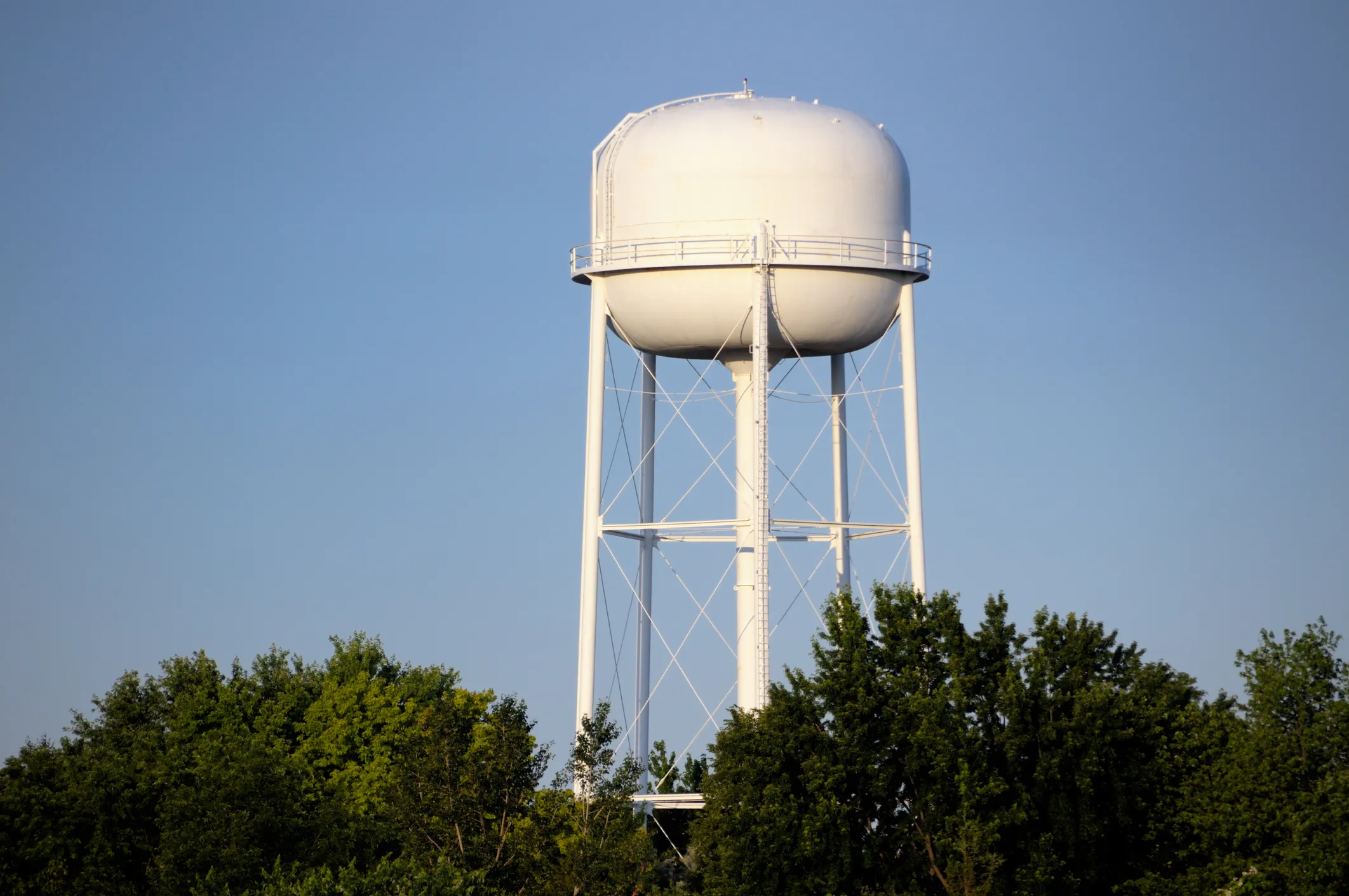 White water tower that follows AWWA C652-2025 storage procedure near green trees.
