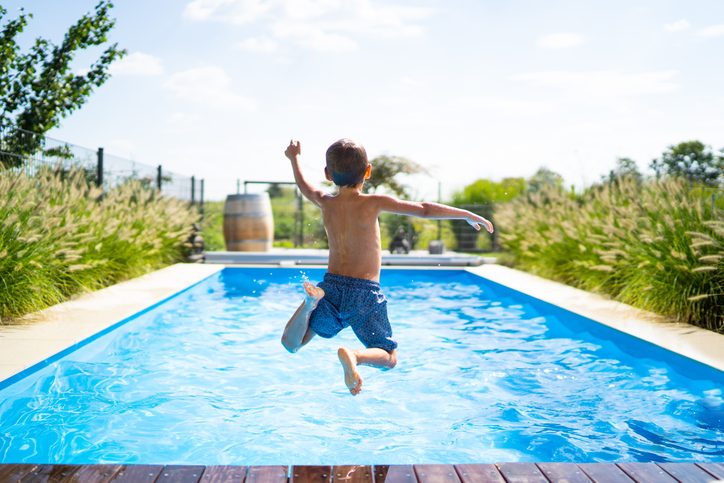 Boy plunging into vacation swimming pool, crystalline blue and heated with an ANSI/ASHRAE 146-2020 pool heater.