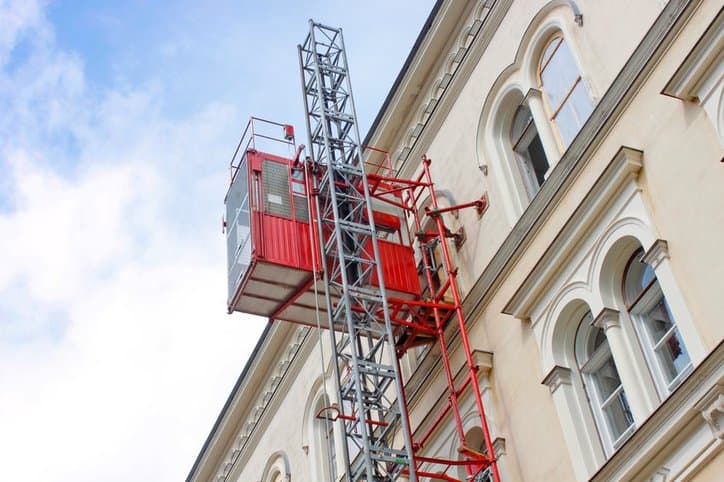 Hoist elevator on the side of a building while following ANSI/ASSE A10.4-2016