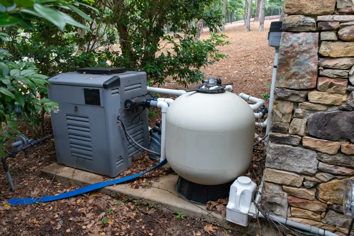 Pool heater pump, tested and rated to ANSI/ASHRAE 146-2020, next to a pool filter in a nice upper-class home.