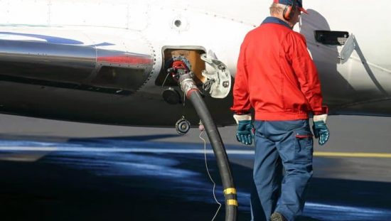 Man in old red windbreaker pumping jet fuel in plane to ASTM D1566-20 specifications.