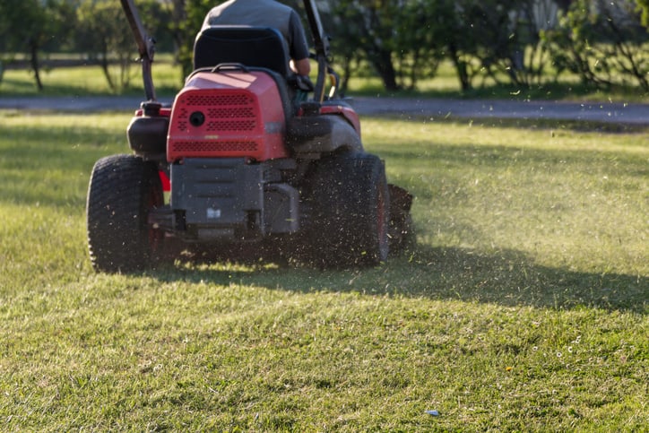 Riding a ANSI/OPEI B71.4 lawnmower to take care of the turf, or grass.