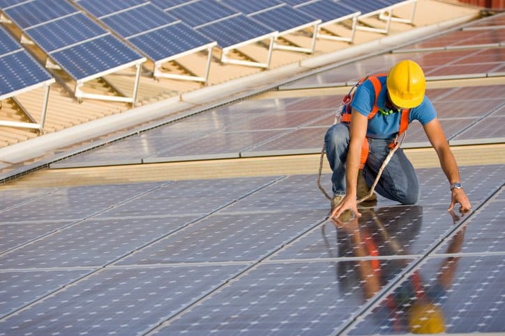Worker in hardhat carefully installing solar photovoltaic (PV) panels that will undergo IEEE C57.159-2016 photovoltaic transformers.