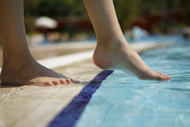 Young girl dipping toe in public pool to test the water quality instead of following ANSI/APSP 11-2019.