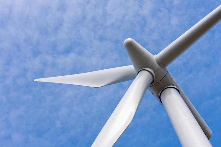 Wind turbine rotor spinning under blue cloudy sky and reachable by an ASME A17.8-2016 wind turbine service elevator.