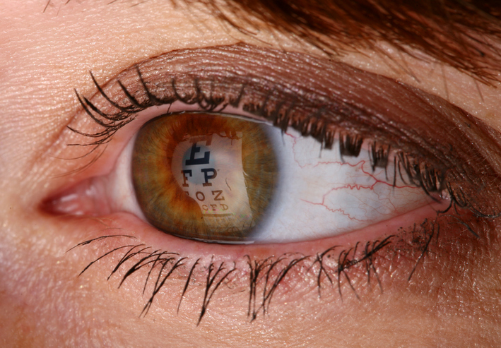 Brown iris during eye exam reflecting optotypes of Snellen chart designed to ANSI Z80.21-2020 to find her visual acuity.