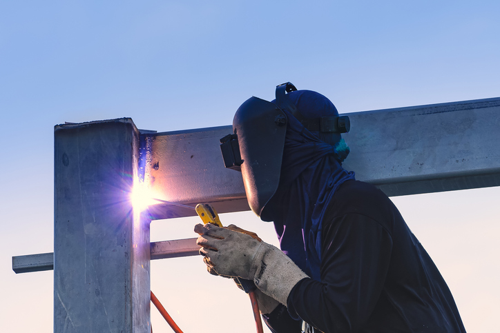 Worker joining metals in building weld while following AWS A2.4:2020 for standard welding symbols.