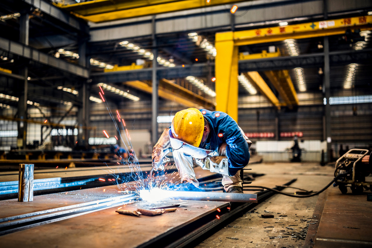 Welder geared up in large warehouse and keeping the difference between welding symbol and weld symbol in mind.