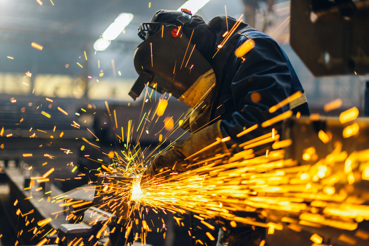 Welder letter sparks fly with a grinder while following the AWS A3.0:2020 standard welding terms.