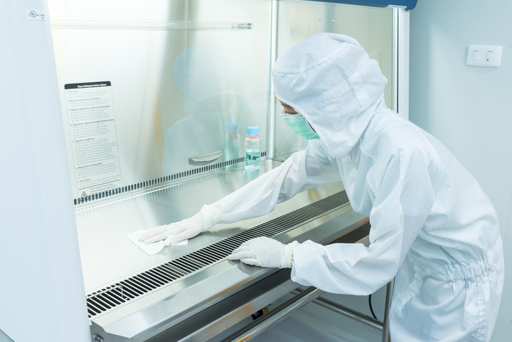 Scientist wearing protective clothing and wiping down biosafety cabinet, struggling with common lab decontamination.
