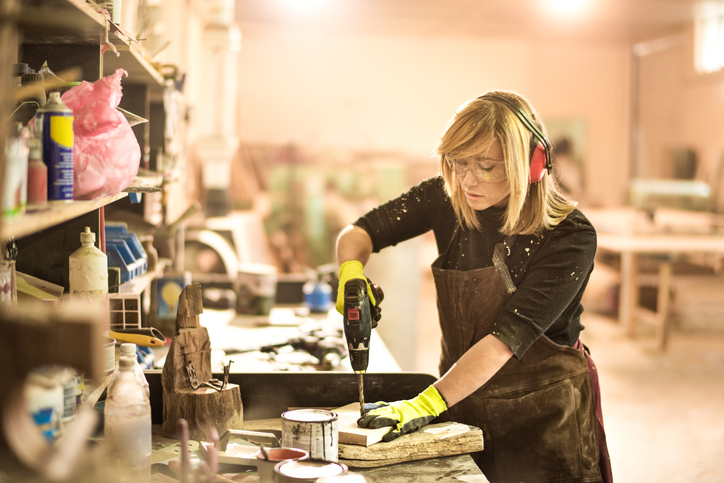 Worker using a drill with proper protection like ear protection that's specified in ANSI/ASA S12.6.