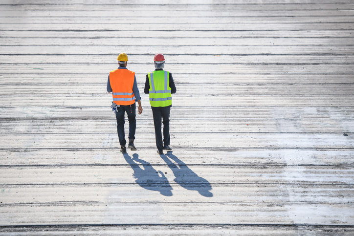 Two construction guys walking on boardwalk from behind and donning ANSI/ISEA 107-2020 high visibility apparel.