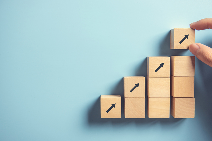 Stacking wood block arrows on blue background to show the quality management progress through ISO 10018:2020 people management.
