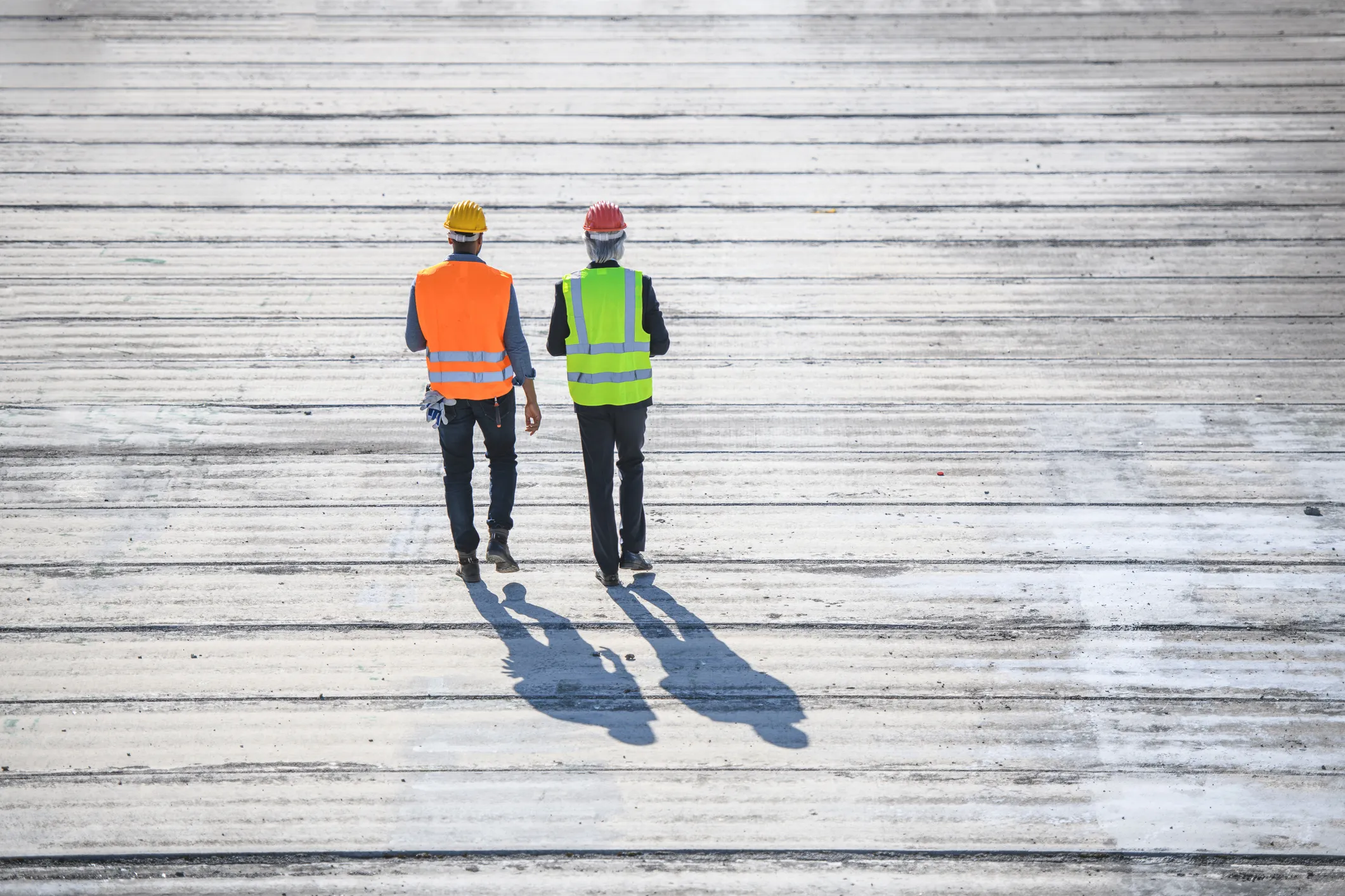 Two construction guys walking on boardwalk from behind and donning ANSI/ISEA 107-2020 high visibility apparel.