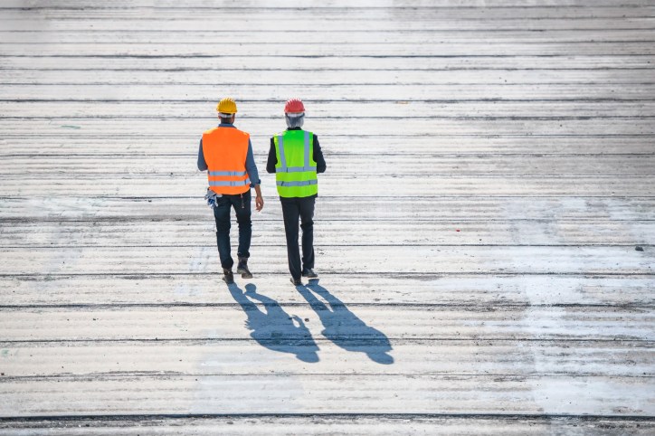 Two construction guys walking on boardwalk from behind and donning ANSI/ISEA 107-2020 high visibility apparel.