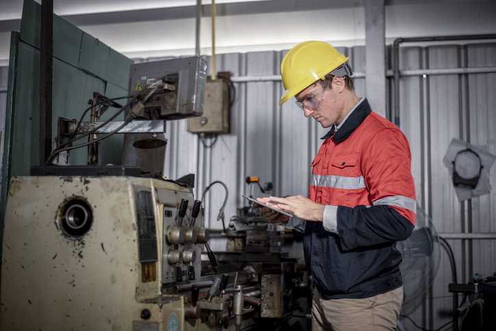 Engineer in yellow hardhat looking at old machinery to prevent hazardous energy.