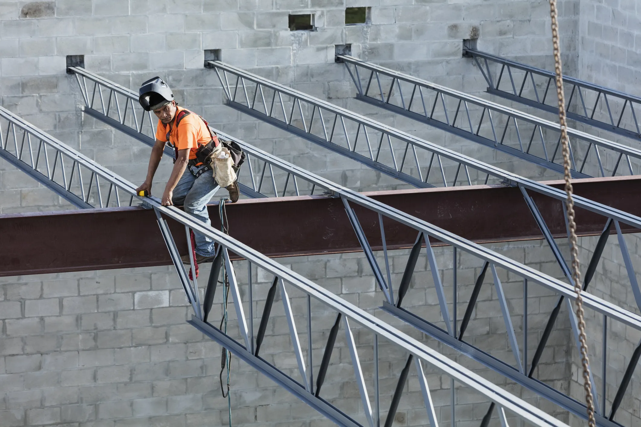 Welder working on metal rafters at height with ANSI/ASSP Z359.1 fall protection requirements.