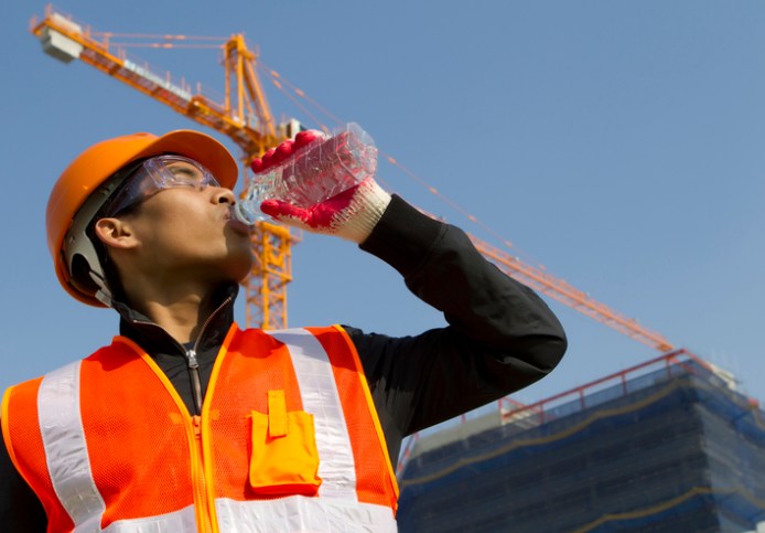 Construction worker in bright yellow HVSA drinking from a water bottle to combat the summer heat.