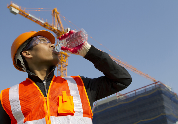 Construction worker in bright yellow HVSA drinking from a water bottle to combat the summer heat.