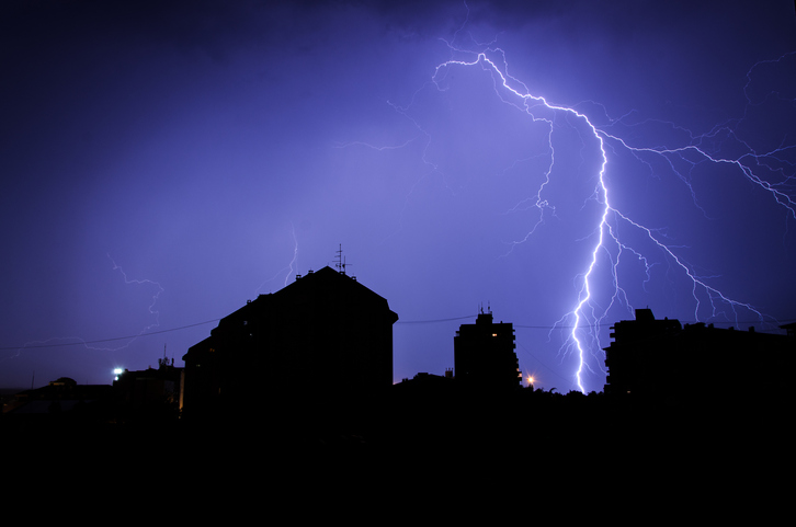 Lightning striking house in blue darkness, prompting need for IEEE C62.41.3-2020 surge protective devices.