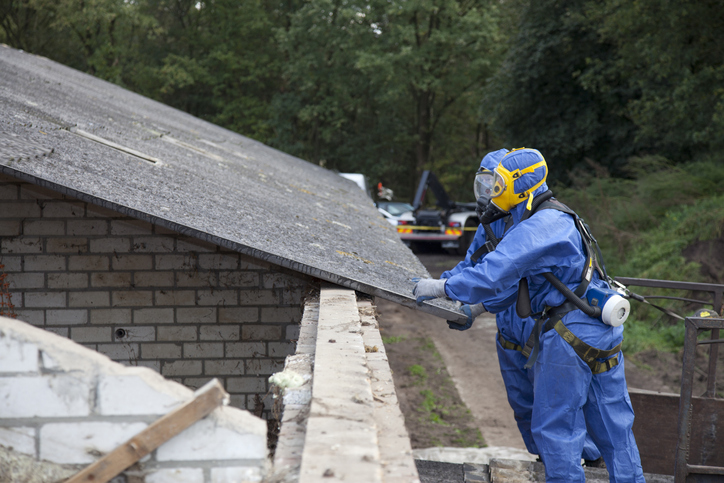 Workers in blue PPE removing asbestos on a dilapidated roof during abatement process.