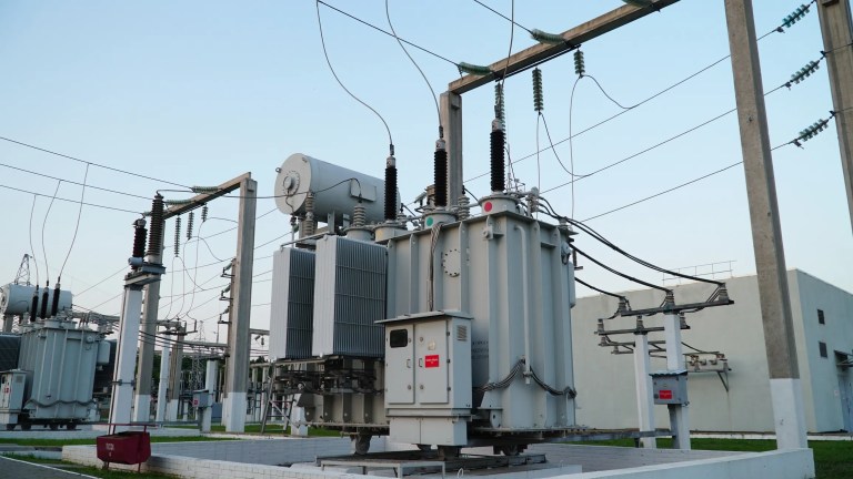 Gray electrical power transformer tested to ANSI/NETA ATS-2025 beneath blue sky