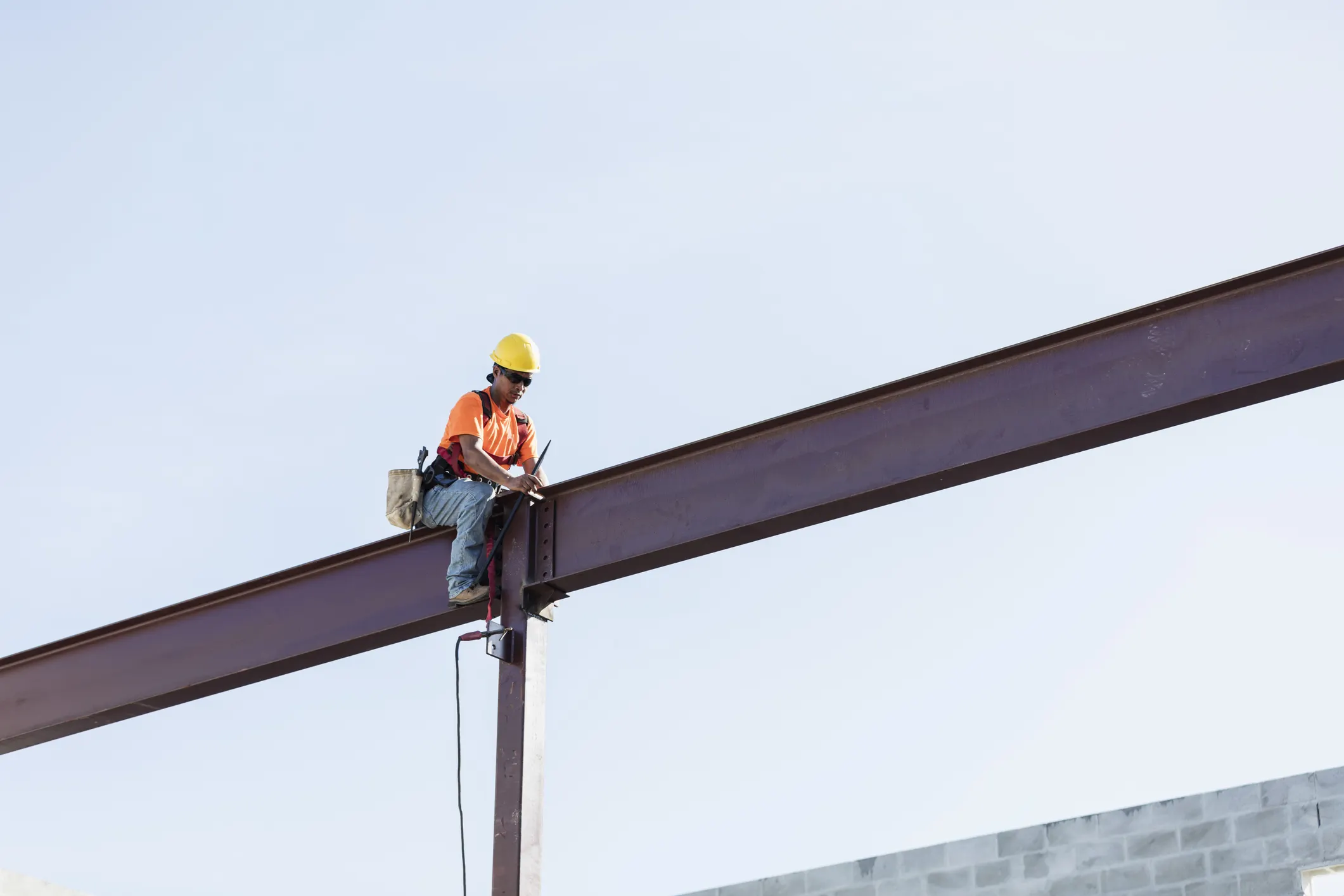 Worker sitting on girder and held safe by ANSI/ASSP Z359.11-2021 full body harness in the sky.