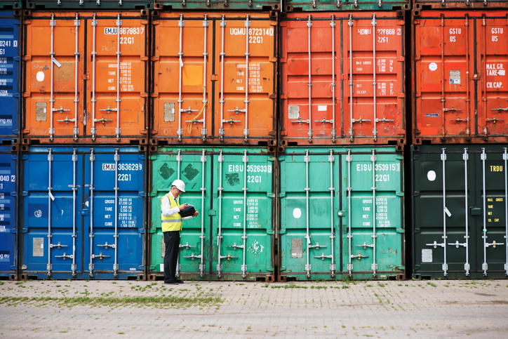 Manager walking beside colorful shipping containers and checking on supply chain security through SCS 9001.