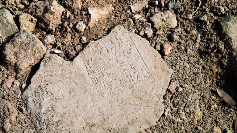 Broken cuneiform tablet in the dirt written in ancient language Akkadian, or in a ISO 639-2 code, akk.