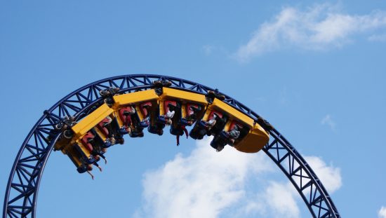 Roller coaster twisting patrons in yellow cars in the sky that was designed by following ASTM F2291-21.