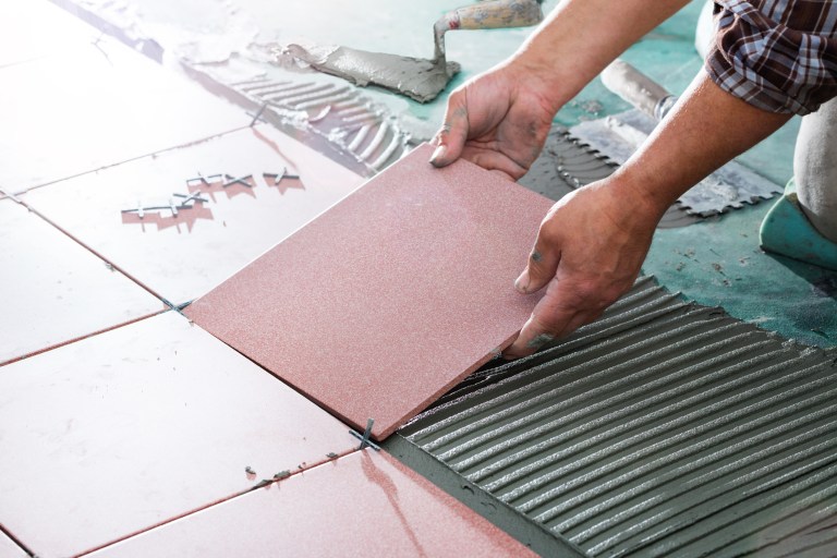 Man installs ceramic tile on floor while following ANSI TCNA guidelines.